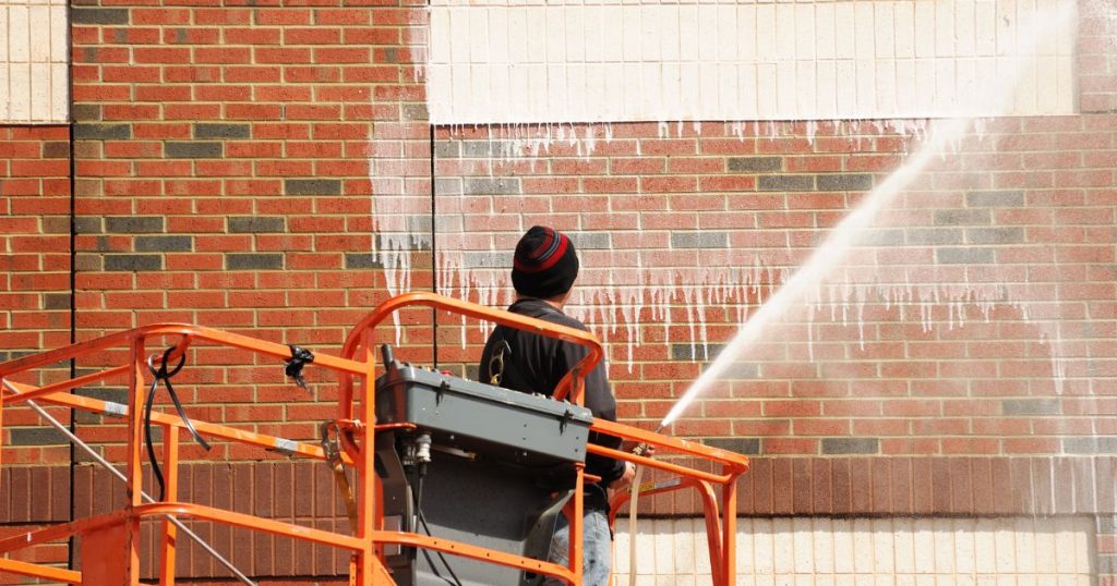 Professionele gevelreiniger reinigt witte crepigevel met hogedrukreiniger vanuit hoogtewerker.