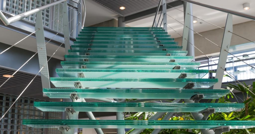 Het frame van de trap is van staal. De traptreden zelf zijn van (groen) glas. Onder de trap staat een grote plant waarvan de bladeren tussen een aantal treden uitsteken.