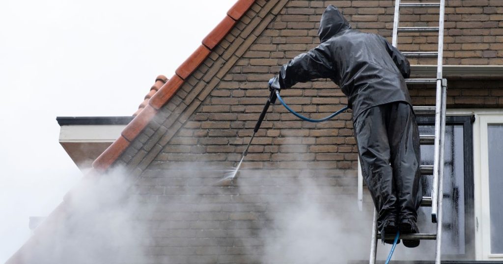 Vakspecialist reinigt rode bakstenen gevel met hogedrukspuit vanaf hoogtewerker