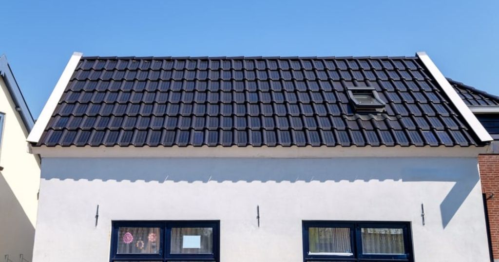 Vrijstaand huis met witte gevel en zonnepannen. In het dak is ook een Velux-raam geïntegreerd.