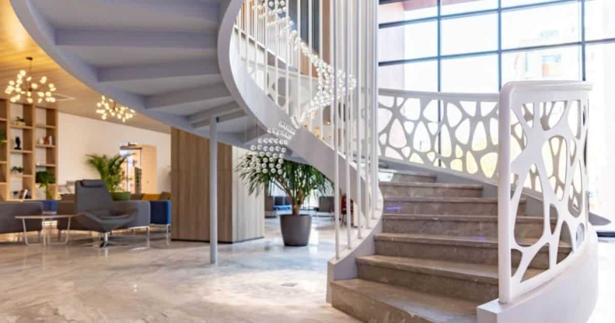 Een witte luxueuze moderne spiltrap met decoratie aan de trapleuning. De trap komt uit op een luxueuze lobby van een kantoor of hotel.