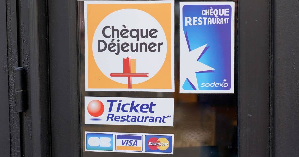 De logo's van aanbieders van maaltijdcheques op de ruit van een glazen deur van een restaurant..