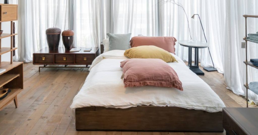 Rustige slaapkamer met donker, mat massief parket. In de slaapkamer staat een twijfelaar met een geel, blauw en twee roze kussens.