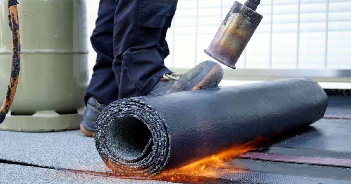Een dakdekker rolt een rol bitumen uit op een plat dak. Hij of zij gebruikt een gasbrander om de roofing of het bitumen te smelten om het zo aan de onderlaag te hechten.