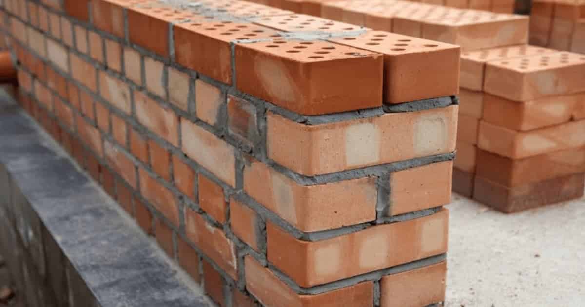 Close-up van een spouwmuur in opbouw met rode bakstenen en zichtbare spouwruimte tussen binnen- en buitenmuur, zonder isolatiemateriaal.