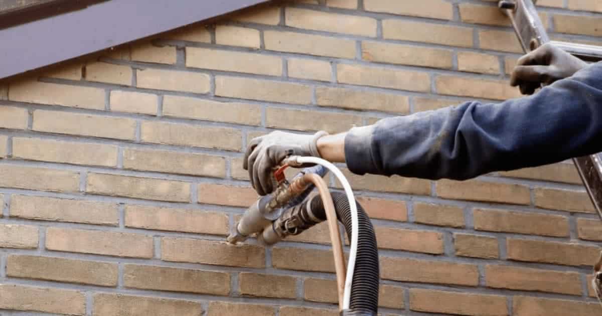 Vakman blaast spouwmuurisolatie in via boorgaten in een Belgische bakstenen gevel.