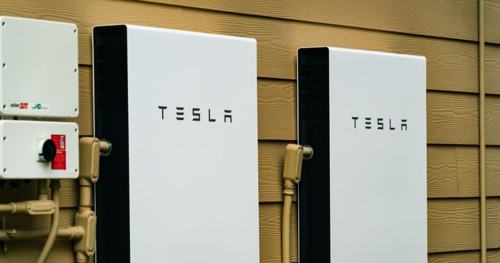 Twee Tesla thuisaccu's naast elkaar aan een houten wand.