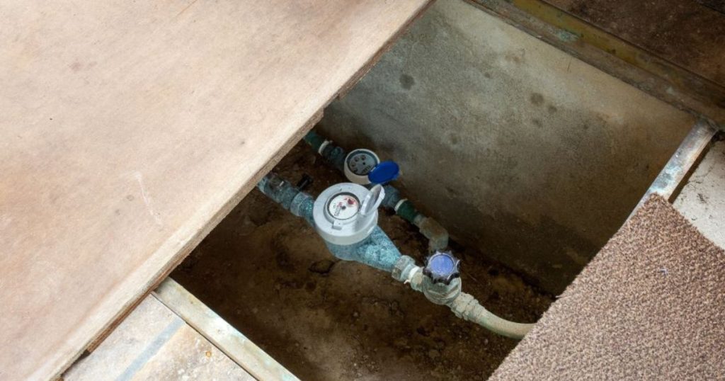 Kruipruimte met watermeter en leidingen zichtbaar onder vloerluik