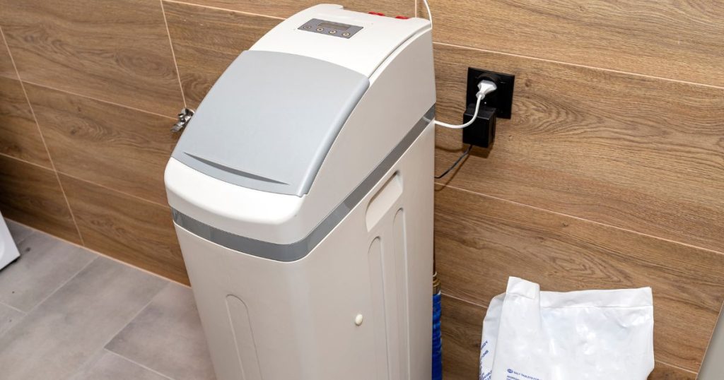 Een compacte waterverzachter op stroom geïnstalleerd tegen een bruine houtkleurige muur. 