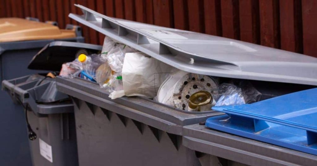 Open afvalbak gevuld met plastic flessen, etensresten en ander afval