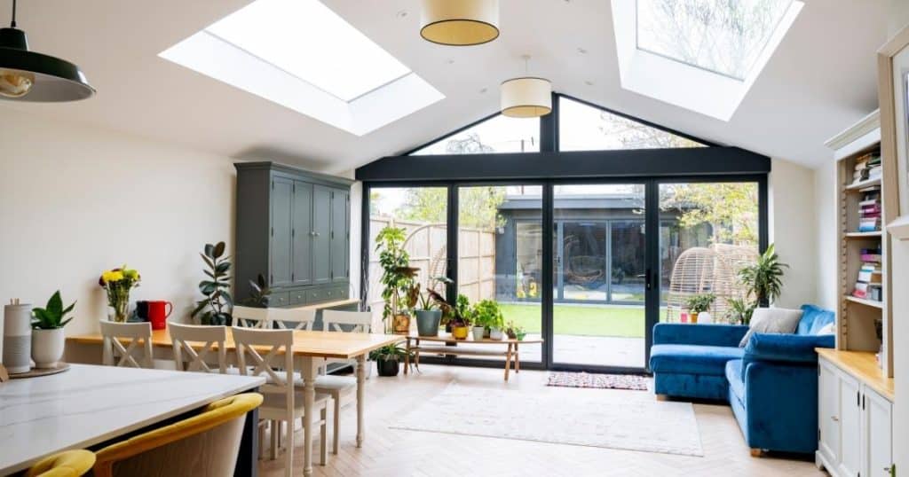 Binnenkant van een woning waaraan een ruime uitbouw werd gebouwd. De uitbouw dient als living en eetruimte, en beschikt over twee grote dakramen en een grote, glazen voorwand met schuifdeuren.