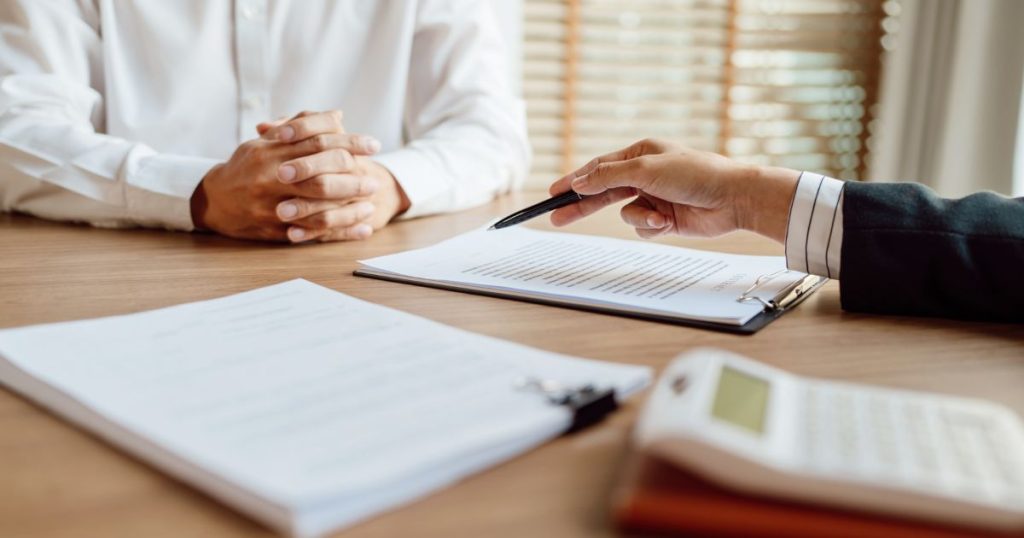 Een verzekeringsexpert zit samen met een ondernemer aan tafel. Ze vergelijken verschillende aansprakelijkheidsverzekeringen voor bedrijven.