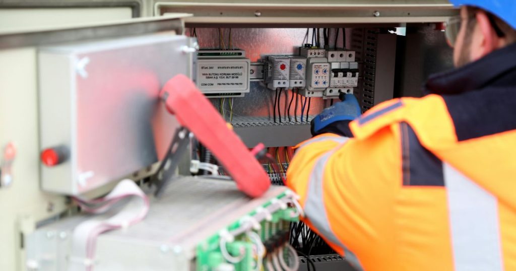 Een installateur in fluo jas is in de weer met een meterkast.
