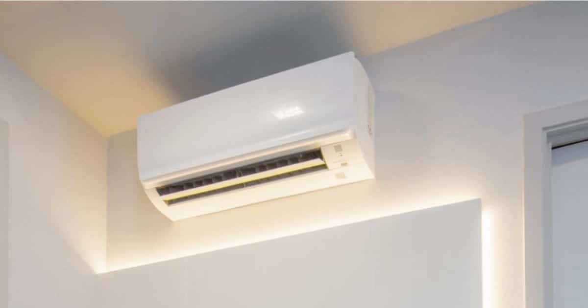 Witte split airco binnenunit gemonteerd hoog aan de muur in een woonkamer, met geopende luchtklep voor koeling of verwarming.