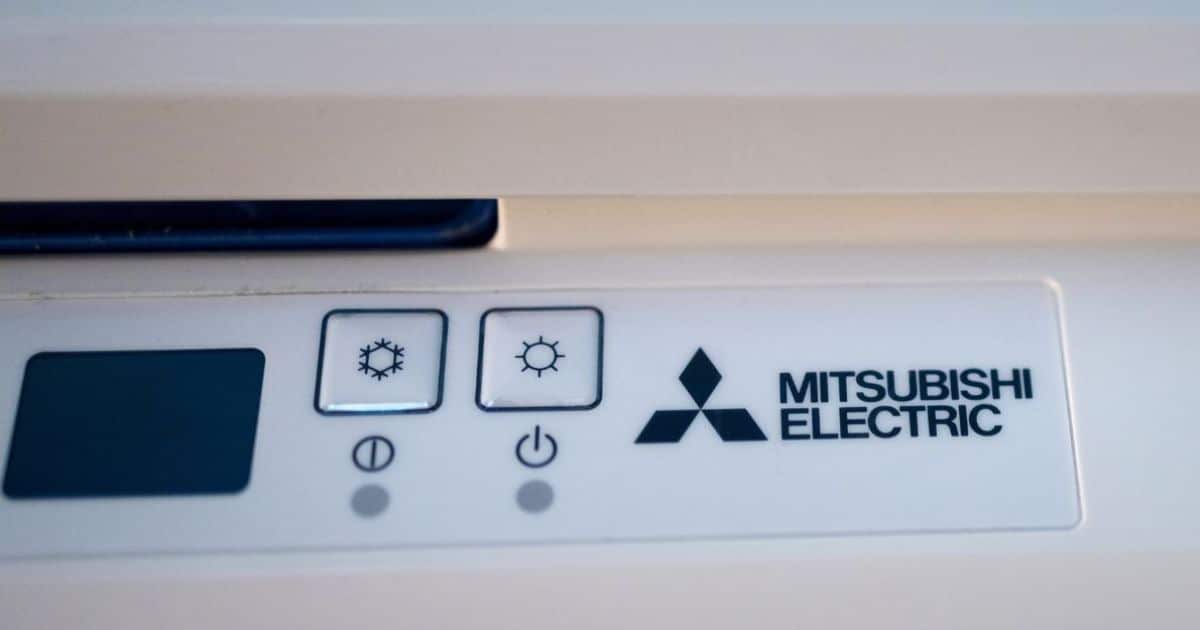 Het logo van Mitsubishi Electric op een witte airconditioner. Naast het logo staan 2 drukknoppen: één met een ijs- of koelicoon en één met een zonnetje.
