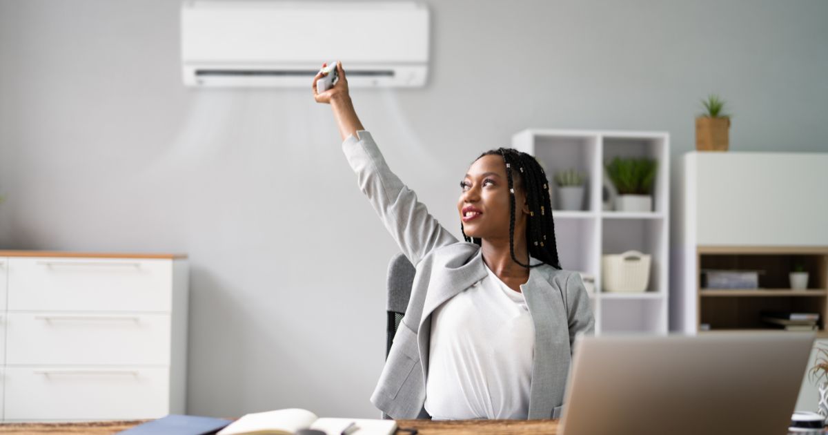 Een vrouw die haar airco aanzet in haar thuiskantoor om rustig te kunnen werken.