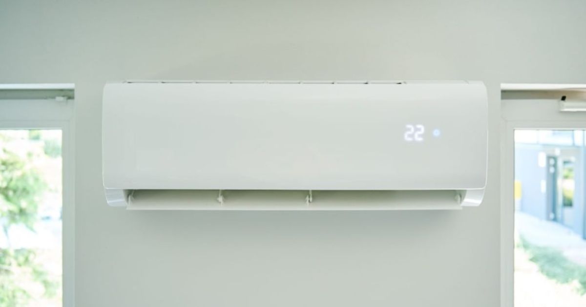 Een witte aircoheater binnenunit tussen 2 ramen, een toestel waarmee je voor een schappelijke prijs je woning kunt koelen en verwarmen. De temperatuur op dit toestel is ingesteld op 22 graden.