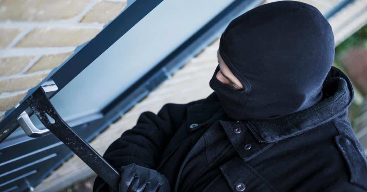 Een inbreker verschaft zich toegang tot een woning met een koevoet. Hij draagt een zwarte jas en zwarte bivakmuts. 