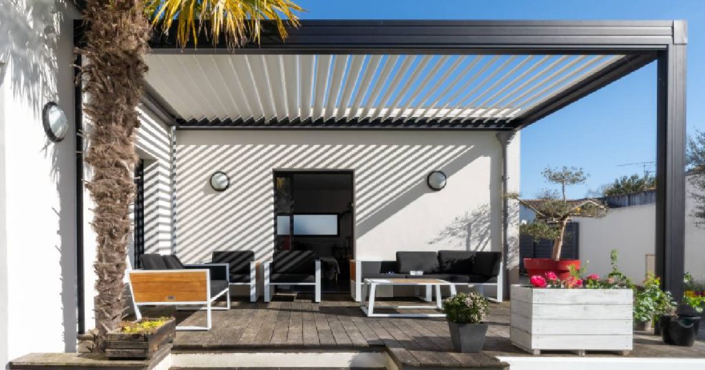 Een zwarte aluminium pergola of open veranda met lamellen zonwering tegen de witte gevel van een woning.