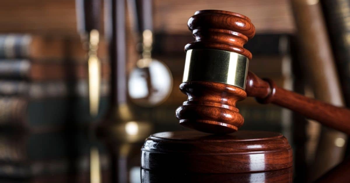 Een glanzende voorzittershamer in donker hout met een roden gloed. Op de achtergrond, vervaagd, liggen stapel met oude boeken.