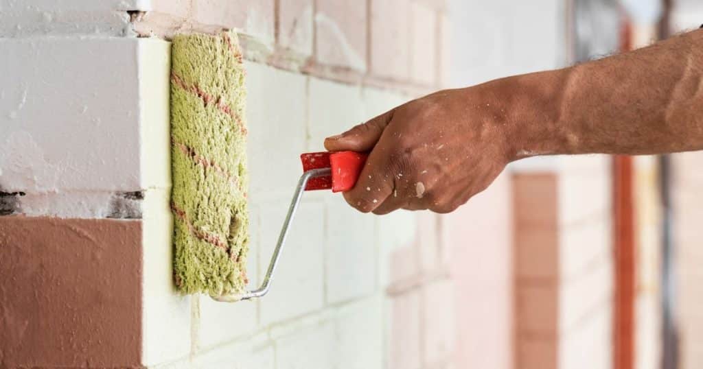 Professionele schilder schildert een bakstenen muur met een verfroller voor een egaal resultaat
