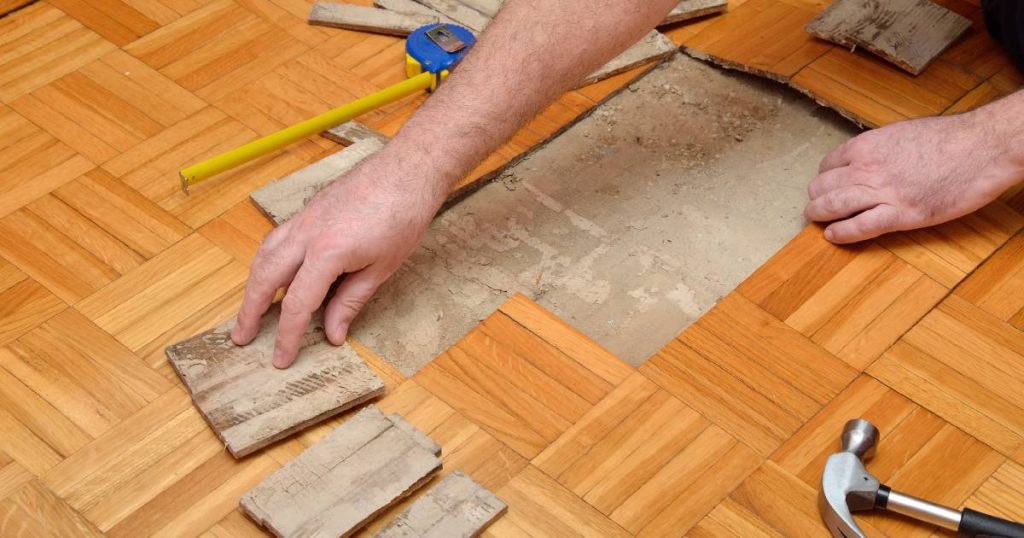Een vakspecialist vervangt beschadigde vloerdelen van een lamelparket. 