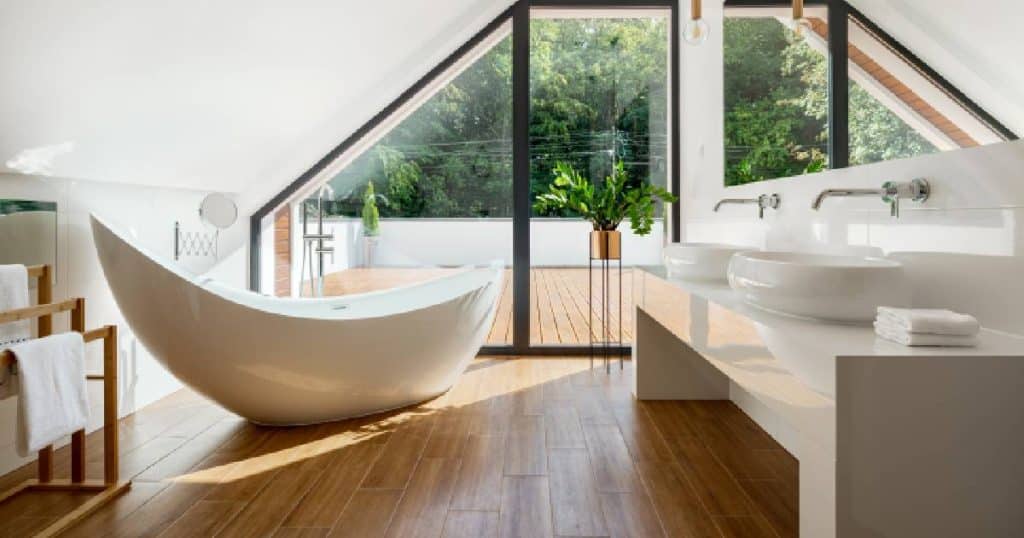 Een stijlvolle badkamer met wit sanitair op een houten vloer. De badkamer heeft een groot raam dat uitgeeft op een terras.