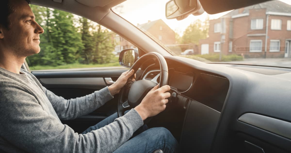 Ontspannen bestuurder achter het stuur van een auto met warm daglicht door de voorruit.