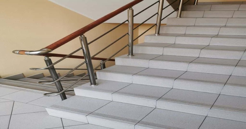 Trappenhuis met wit-beige tegeltrap: de trapleuning is van metaal.