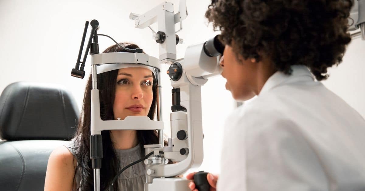 Een oogarts met bruine krullen en een wit hemd onderzoekt de ogen van een patiënte met stijl bruin haar.