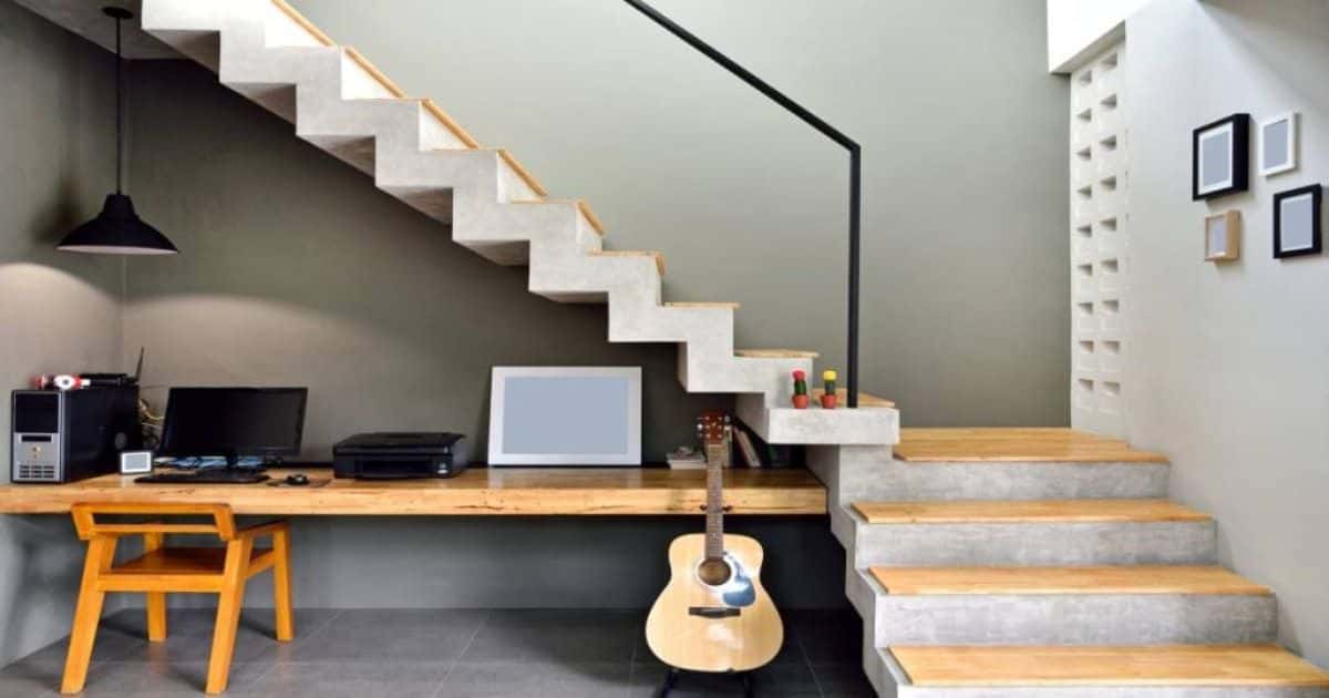 Een betonnen trap met pvc trapcovers in houtlook. Onder de trap werd een bureautje ingericht met een houten tafel, houten bureaustoel, computer en klassieke gitaar.
