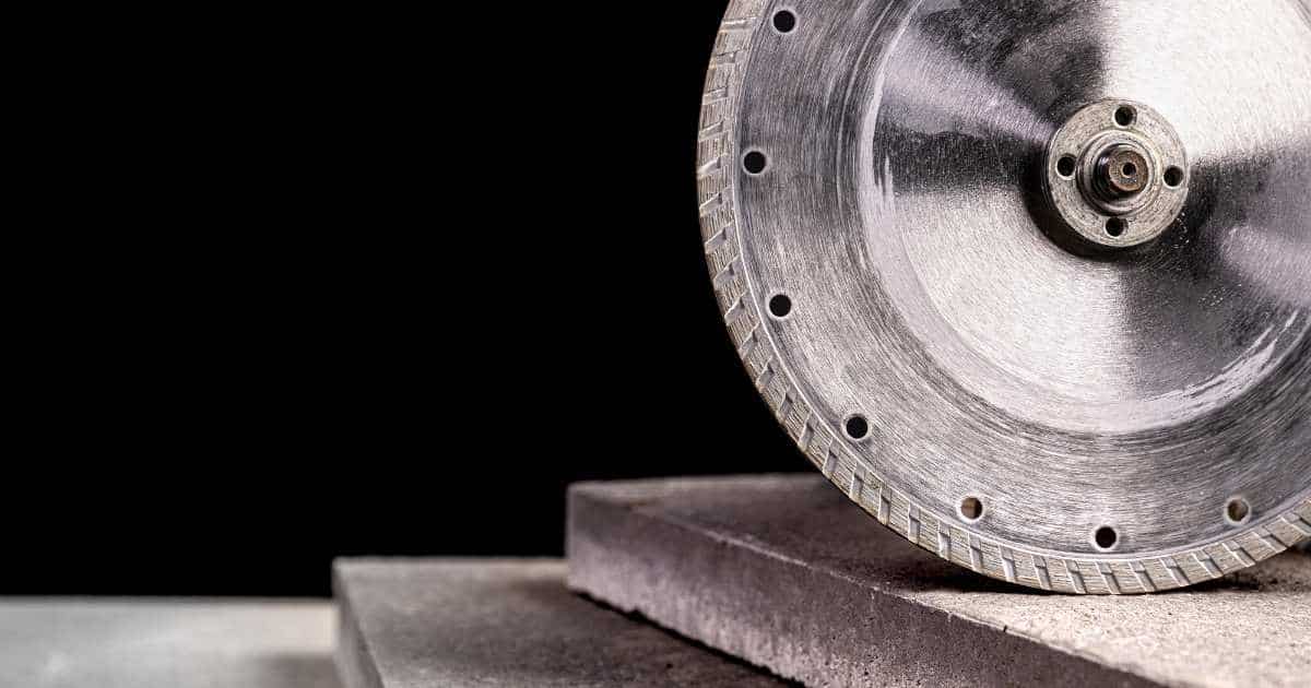 Een betonzaag tegen een zwarte achtergrond, op twee betonnen tegels.