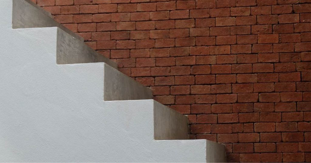 Een betonnen trap tegen een oranje bakstenen muur. Men heeft de trap wit laten schilderen.