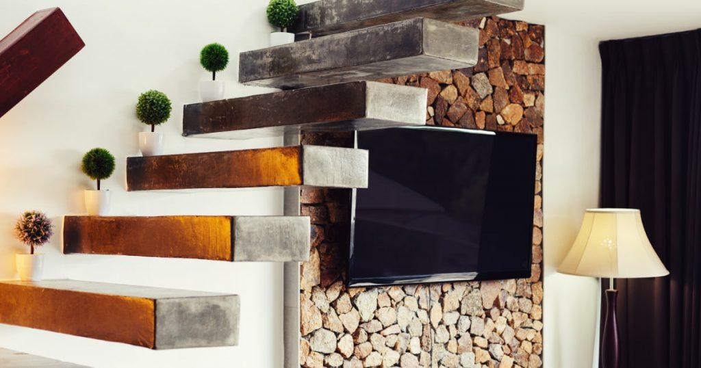 Zwevende, donkere betonnen trappen. Aan de muur hangt een tv tegen een houten achterwand. Op de trap zelf staan miniplantjes ter decoratie.