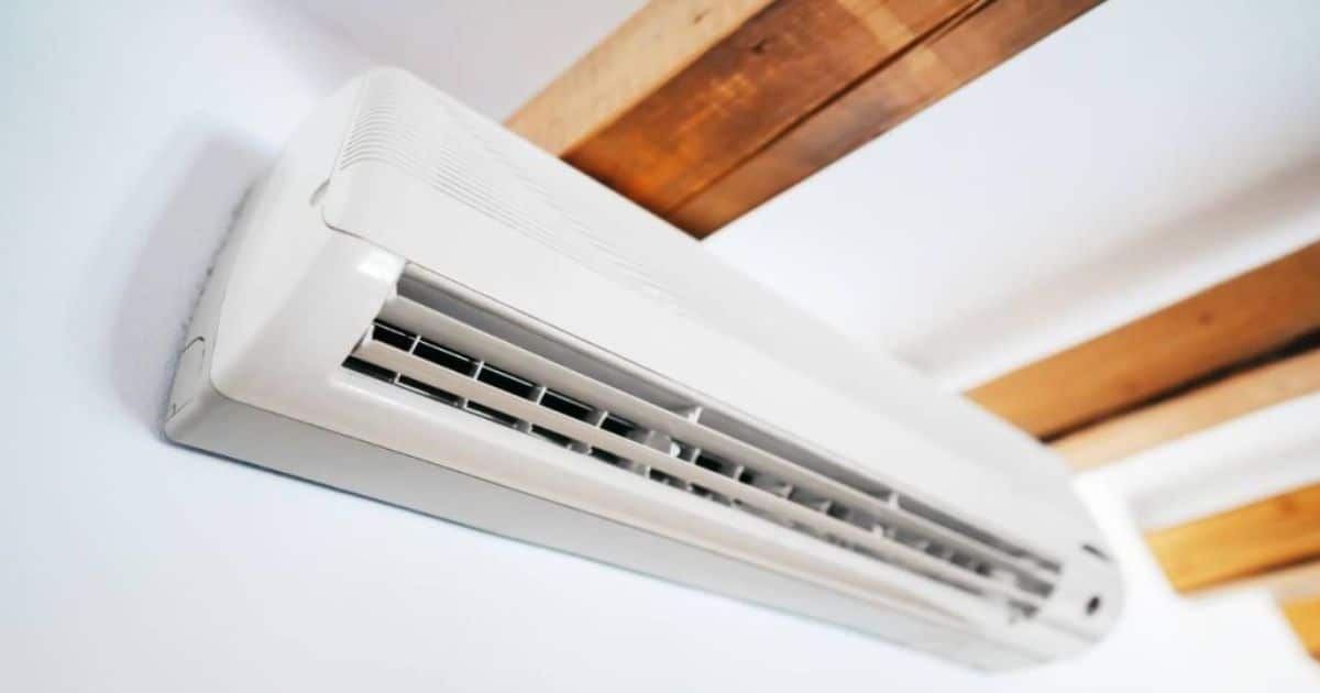 De binnenunit van een split-airco systeem met hoog rendement tegen een witte muur, net onder een wit plafond met zichtbare houten balken.
