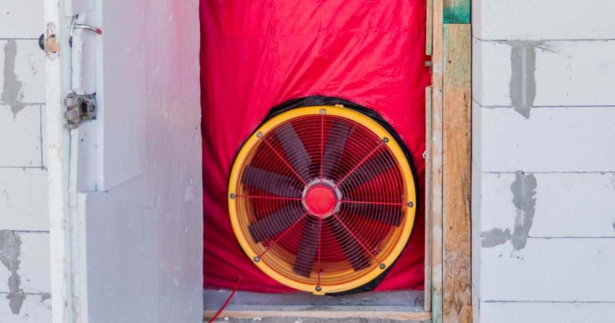 Ventilator in een deuropening met rood doek tijdens een blowerdoortest voor luchtdichtheid van een gebouw.