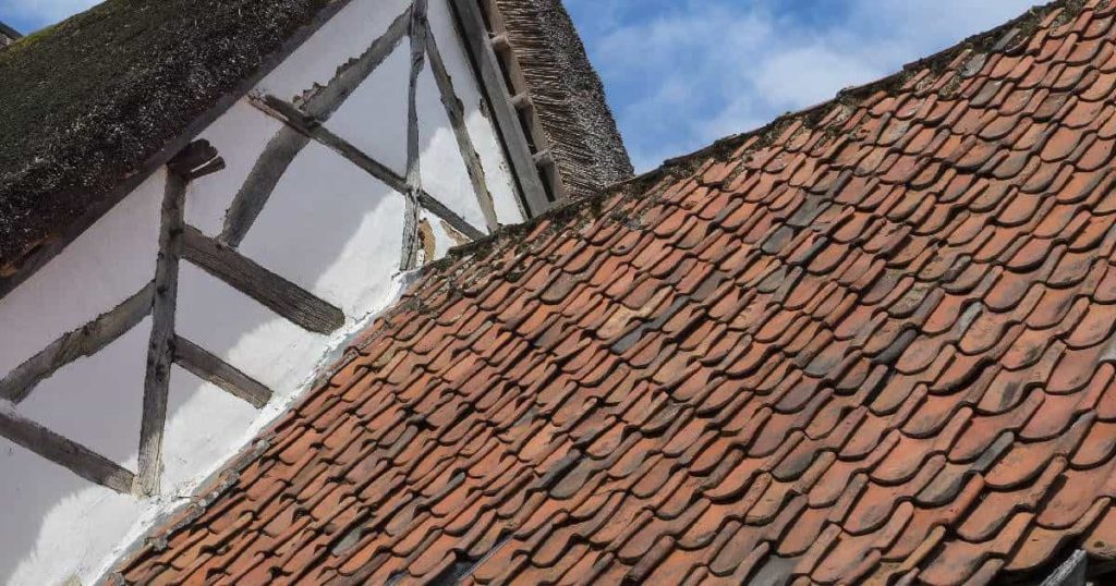 Dak van een oude woning met gevel in leem en verweerde, boomse dakpannen. De donkere sporen van slijtage verraden hun ouderdom.