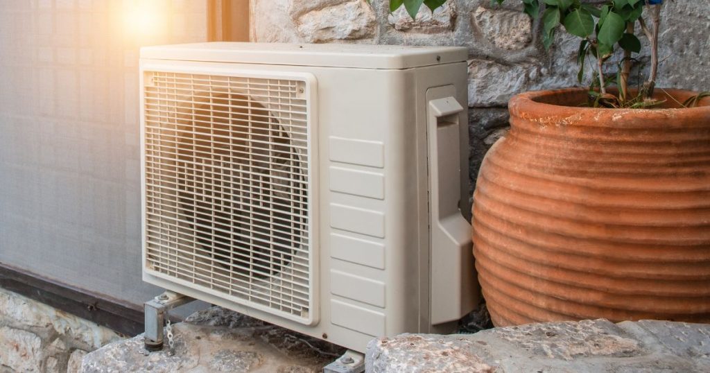 Buitenunit van een warmtepomp naast stenen gevel en grote terracotta pot bij een woning die in aanmerking komt voor een premie