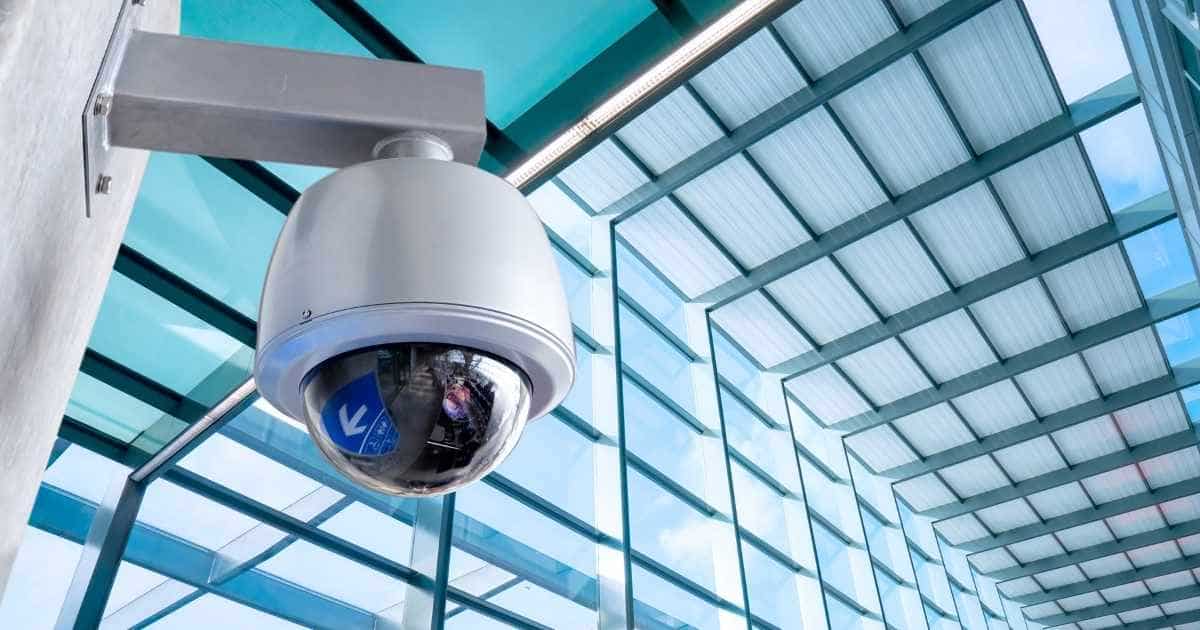 Eem dome-camera met glazen koepel hangt in een grote, glazen bedrijfshal.