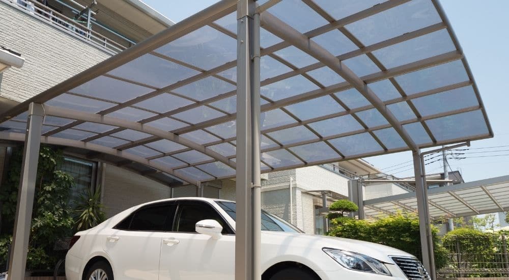Een BOzARC carport met gebogen dak uit polycarbonaat en aluminium frame. Onder de carport staat een witte auto.