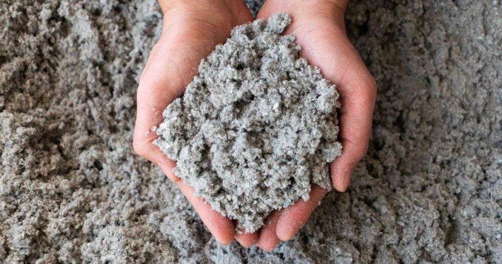 Twee handen met een hoopje cellulose isolatie of papiervlokken, met daaronder een massa cellulosevlokken.