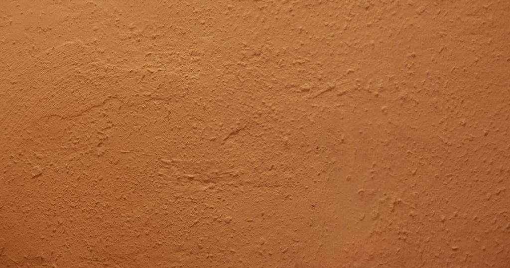 Detailbeeld van een gevel bekleed met oranje cementpleister met ietwat grove, korrelige textuur.