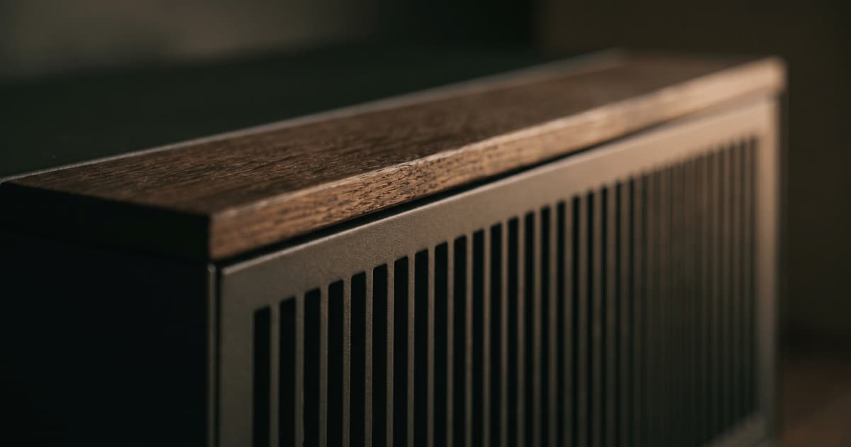 Een detailopname toont een donkere houten omkasting met fijne verticale ventilatielamellen en een brede afwerkrand in donker hout met zichtbare nerf.