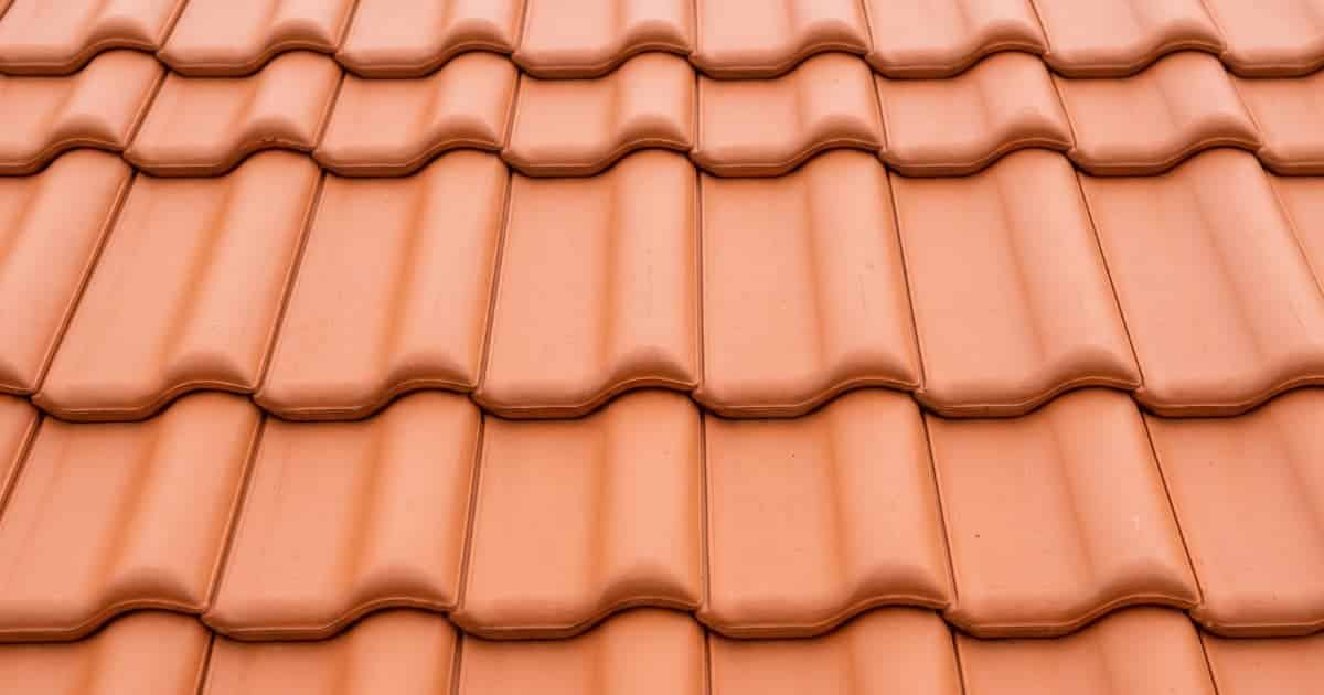 Rijen golvende keramische dakpannen in een uniforme terracotta kleur liggen strak over elkaar op een hellend dak onder zacht daglicht.