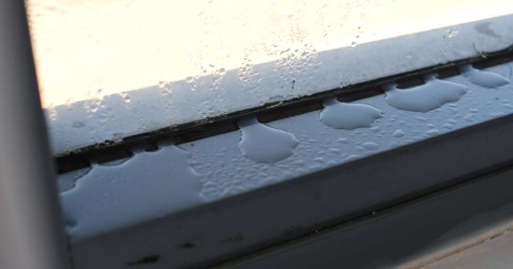 Een raam in een veranda met condens. De druppels verzamel zich op de onderkant van het raamkader.