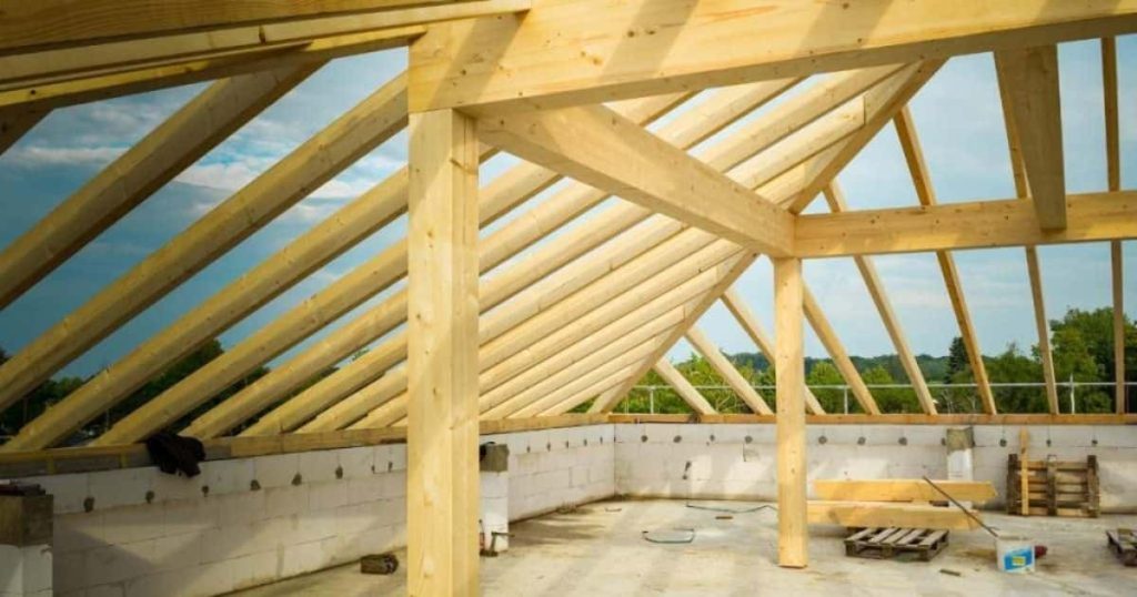 Een houten dakgebinte rust op een betonnen structuur. Op de zoldervloer liggen verspreid werkmaterialen.