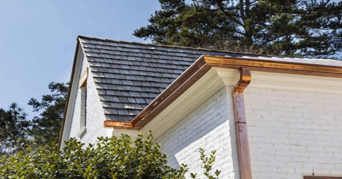 Koperen dakgoot en -afvoer aan een leien dak en een woning met witte bakstenen.