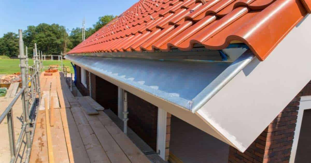Installatie van een dakgoot in zink aan een nieuw dak met rood-oranje dakpannen.