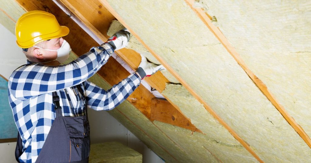 Een dakisolatiespecialist plaatst dakisolatie onder een hellend dak. Dakisolatie is sinds 2020 verplicht voor alle zelfstandige woningen in Vlaanderen.