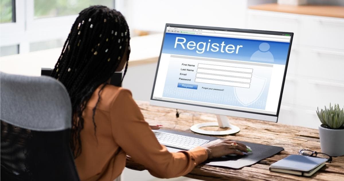 Een werknemer met zwart haar en een oranje hemd zit achter een computerscherm dat op een houten tafel staat. Ze meldt zich aan via het portaal van haar werkgever.